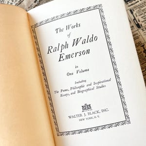 May include: A vintage book cover with a black and white ornate border. The title reads "The Works of Ralph Waldo Emerson in One Volume" and includes the text "Including The Poems, Philosophic and Inspirational Essays, and Biographical Studies". The publisher is Walter J. Black, Inc. New York, N.Y.