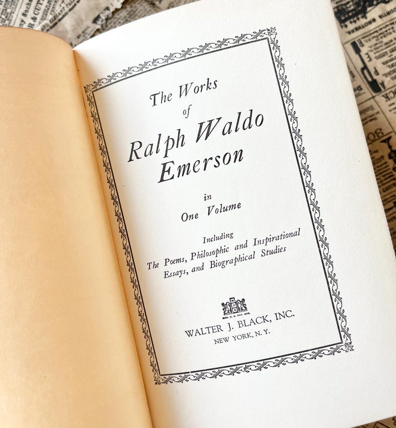 May include: A vintage book cover with a black and white ornate border. The title reads "The Works of Ralph Waldo Emerson in One Volume" and includes the text "Including The Poems, Philosophic and Inspirational Essays, and Biographical Studies". The publisher is Walter J. Black, Inc. New York, N.Y.