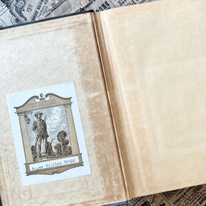 May include: A book with a brown leather cover and a bookplate that reads "Ex Libris Roger William Grupp". The bookplate features a black and white illustration of a man in a hat and coat holding a stick.