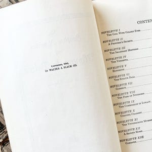 May include: A book titled "The Girl With Golden Eyes" by Balzac. The book cover is white with black text. The book is open to the contents page, which lists the titles of the novellas in the book.
