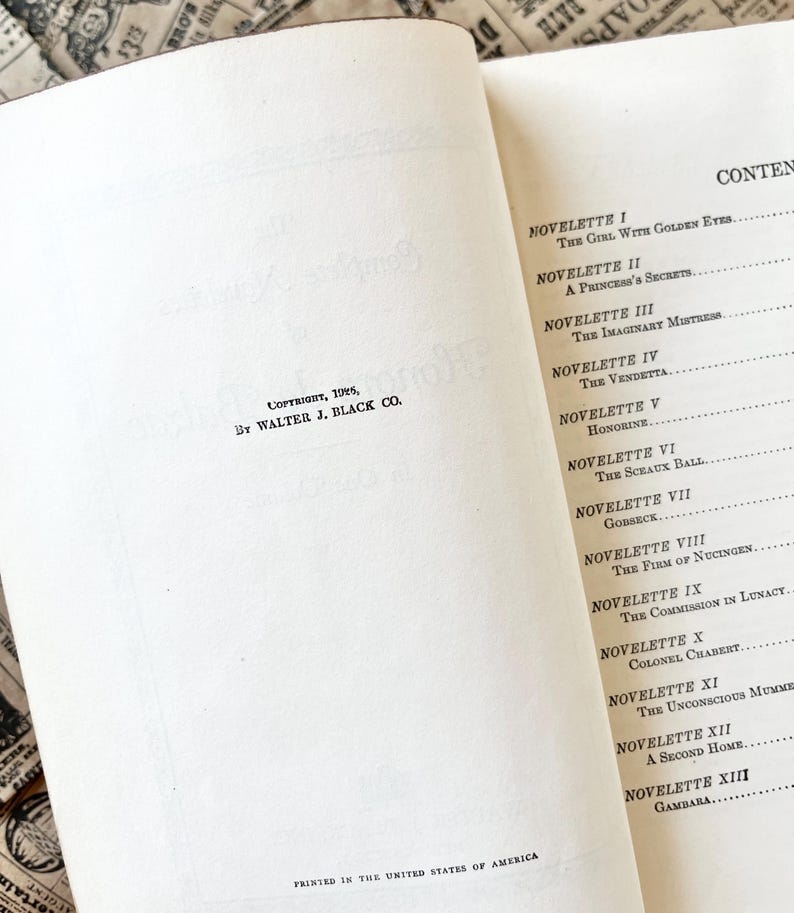 May include: A book titled "The Girl With Golden Eyes" by Balzac. The book cover is white with black text. The book is open to the contents page, which lists the titles of the novellas in the book.
