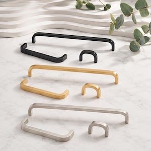 May include: A collection of cabinet hardware including long pulls, shorter handles, and small knobs in matte black, brushed gold, and brushed silver finishes. Each piece features a smooth, rounded U-shaped design with clean lines and a consistent metallic texture.