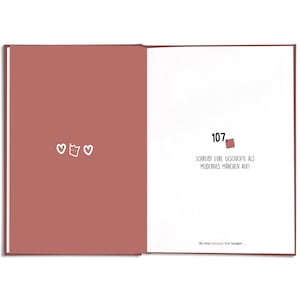 May include: Open book with a red-brown cover and white pages. The left page has three white heart illustrations. The right page has the number 107, a stamp illustration, and German text: SCHREIBT EURE GESCHICHTE ALS MODERNES M&Auml;RCHEN AUF!