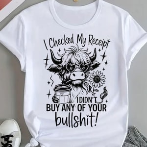 May include: White t-shirt with a graphic of a Highland cow wearing heart-shaped sunglasses, holding a coffee cup and a sunflower. Text reads "I CHECKED MY RECEIPT I DIDN'T BUY ANY OF YOUR bullshit!"