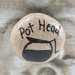 May include: A painted rock with the words "Pot Head" and a black and white illustration of a coffee pot.