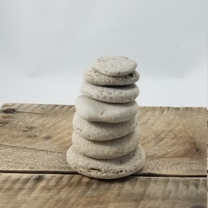 May include: A stack of seven light gray, round, textured stones on a wooden surface.