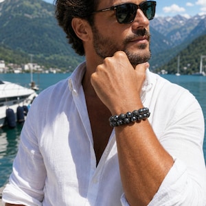 May include: A double-strand beaded bracelet featuring alternating dark grey metallic spheres and textured matte black spherical beads. The bracelet is worn on a wrist, showcasing a combination of polished and porous bead finishes in a circular design.
