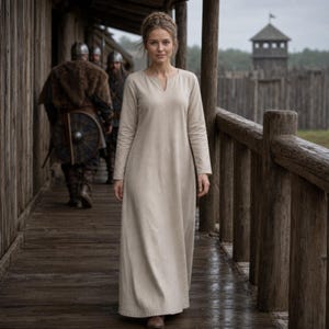Pode incluir: Um vestido bege de manga comprida até aos pés com um decote redondo simples e uma pequena abertura vertical no centro. A peça apresenta um tecido liso de cor sólida e uma silhueta reta e fluida que chega até aos tornozelos.