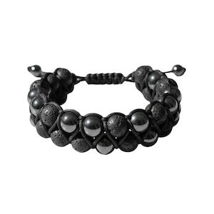 Könnte beinhalten: Ein zweireihiges Armband mit abwechselnden schwarzen, porösen Lavasteinperlen und glatten, reflektierenden metallischen Hämatitperlen. Die Perlen sind mit einer schwarzen Kordel verflochten und das Armband hat einen verstellbaren Schiebeknoten.