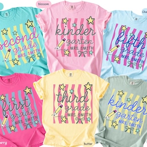 May include: Six short-sleeved crew neck t-shirts in mint, blossom, chambray, crunchberry, butter, and bay colors. Each shirt features a graphic with vertical wavy stripes, a pencil, stars, a bow, and text indicating grade levels and Mrs. Smith.