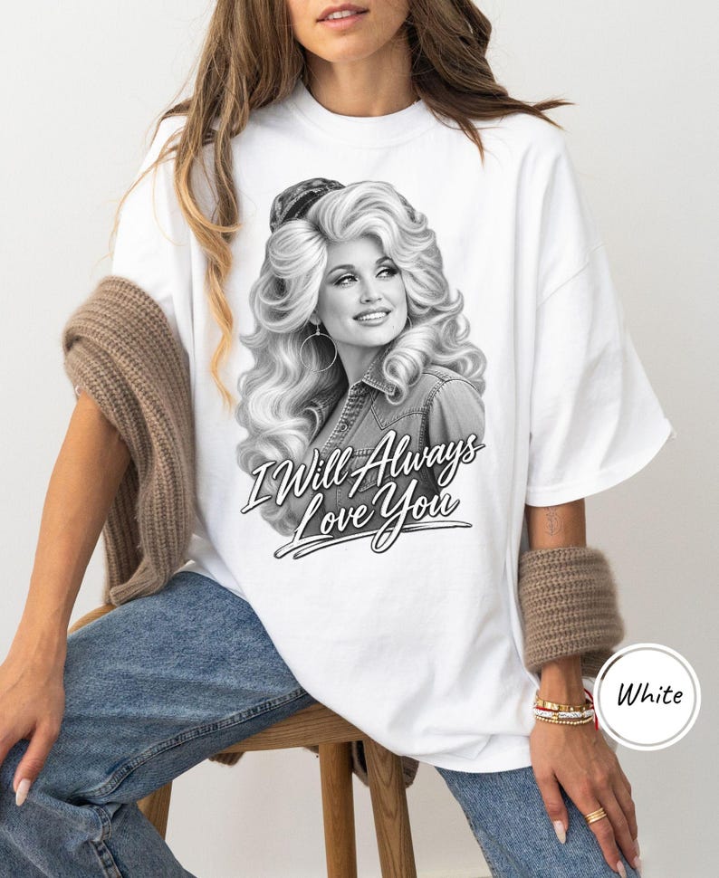 May include: A white t-shirt featuring a black and white graphic print of a woman with voluminous blonde hair, wearing hoop earrings and a denim shirt. Below the portrait, the text reads "I Will Always Love You" in a stylized script font.