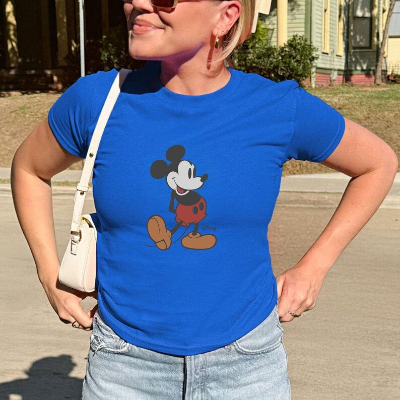 Puede incluir: Una camiseta azul real con un gr&aacute;fico de Mickey Mouse caminando. Mickey se muestra con una cabeza negra, pantalones cortos rojos y zapatos marrones. La camiseta es de manga corta.