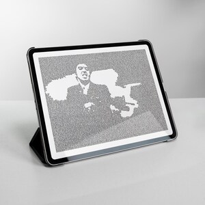 Op de afbeelding: Een zwarte tablet op een zwarte standaard toont een grijswaardenafbeelding van een man in een pak. De afbeelding is samengesteld uit kleine puntjes, wat een textuureffect creëert. De tablet staat op een wit oppervlak.