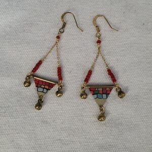 May include: A pair of gold earrings with red beads and a triangular pendant with a colorful mosaic design. The pendant is accented with small gold bells.