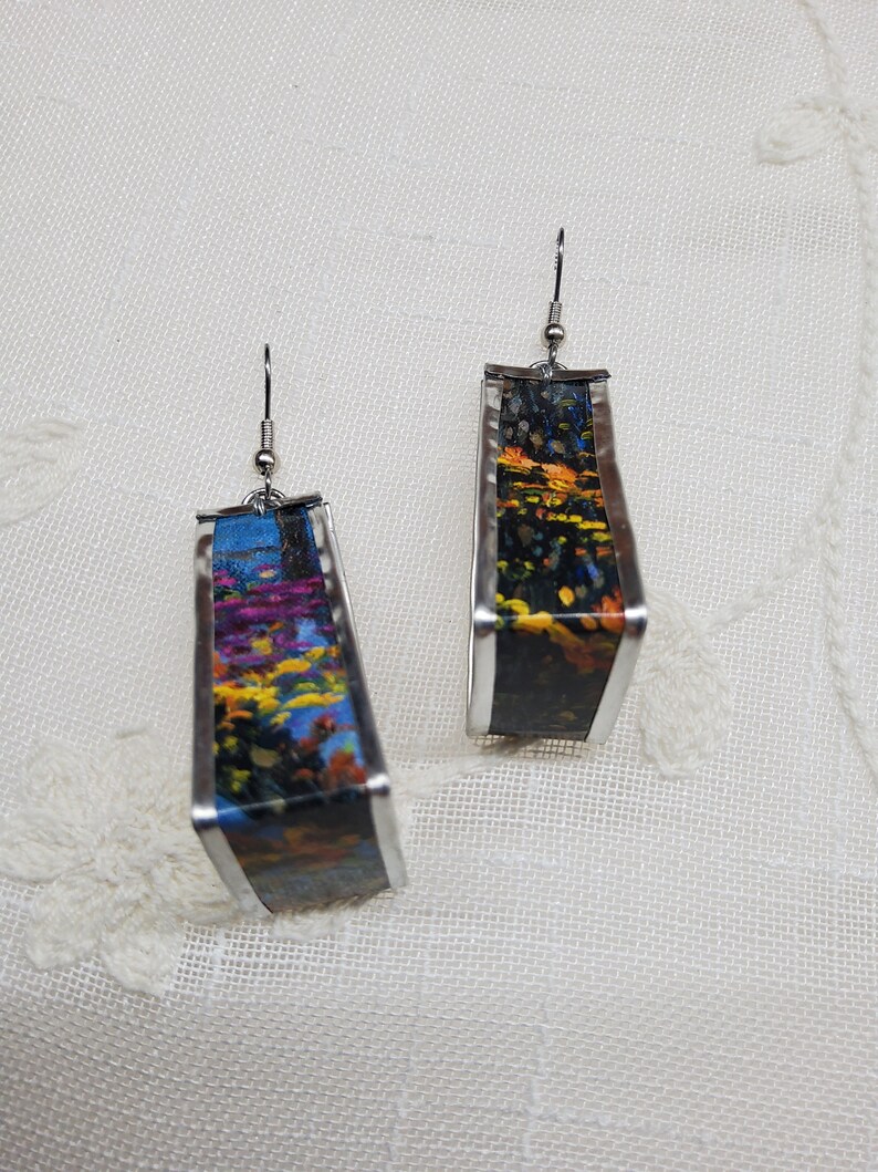 May include: A pair of silver earrings with a rectangular shape. The earrings are decorated with a colorful floral pattern on a black background.