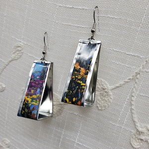 May include: A pair of silver earrings with a rectangular shape. The earrings are decorated with colorful abstract floral patterns.