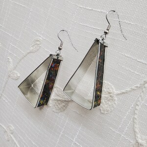 May include: A pair of silver triangle earrings with a colorful abstract design on the inside of the triangle.