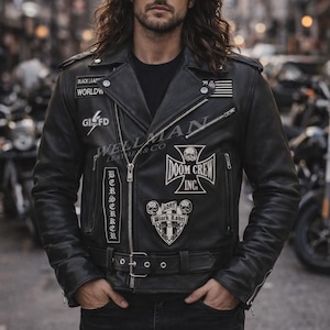 Puede incluir: Chaqueta de cuero negra de motociclista con múltiples parches, cremalleras y cinturón. Los parches incluyen texto y diseños de calaveras. La chaqueta se usa con una camiseta negra y jeans. La imagen se toma al aire libre.