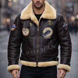 May include: A brown leather jacket with a cream-colored shearling collar and cuffs. The jacket features multiple patches and a zipper closure. The text "WELLMAN LEATHER & CO" is visible on the jacket.