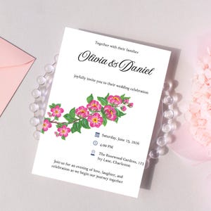 May include: A white wedding invitation with floral accents. The invitation reads "Olivia & Daniel" and includes the date, time, and location of the wedding. Pink flowers and green leaves decorate the bottom of the invitation.