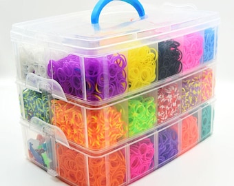 May include: A clear plastic storage container with a blue handle, filled with colorful rubber bands. The bands are organized into compartments, showcasing a variety of colors including pink, purple, yellow, and green. The container is designed for crafting and DIY projects.