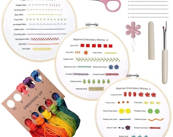 May include: Embroidery kit with three wooden hoops displaying beginner stitch examples, a rainbow of embroidery floss, pink scissors, needles, and other tools. The hoops show various stitches like running, cross, and herringbone.