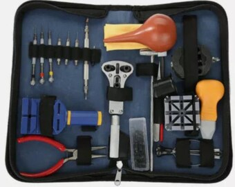 May include: A blue zippered case containing a watch repair tool kit. The kit includes various screwdrivers, pliers, a case opener, a rubber air blower, and other tools for watch maintenance and repair.