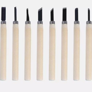 May include: A collection of ten wood carving tools, each with a different blade profile. They feature light-coloured wooden handles and dark metal blades. The tools are displayed in a line, highlighting their diverse cutting edges. The handles are approximately 15 cm long.