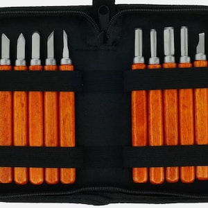 May include: A set of wood carving tools in a black zipped case. The tools have wooden handles and metal blades of various shapes. The case has two sections with elastic straps to hold the tools securely.