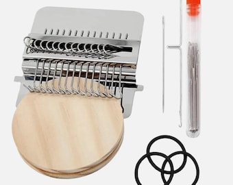 May include: A metal darning loom tool with a round wooden base, featuring a series of silver hooks. Included are two long metal needles, a clear plastic tube containing multiple sewing needles, and three black rubber bands for securing fabric.