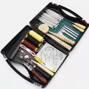 May include: Open black case containing leather crafting tools. Includes various metal tools, wooden handles, spools of thread in yellow, black, and brown, and a cutting mat. The case is open, displaying the assortment of tools.