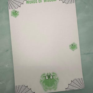 May include: A white notepad with the words "WORDS OF WISDOM" in green at the top. The notepad features green fuzzy spider illustrations and black spiderweb corner designs.