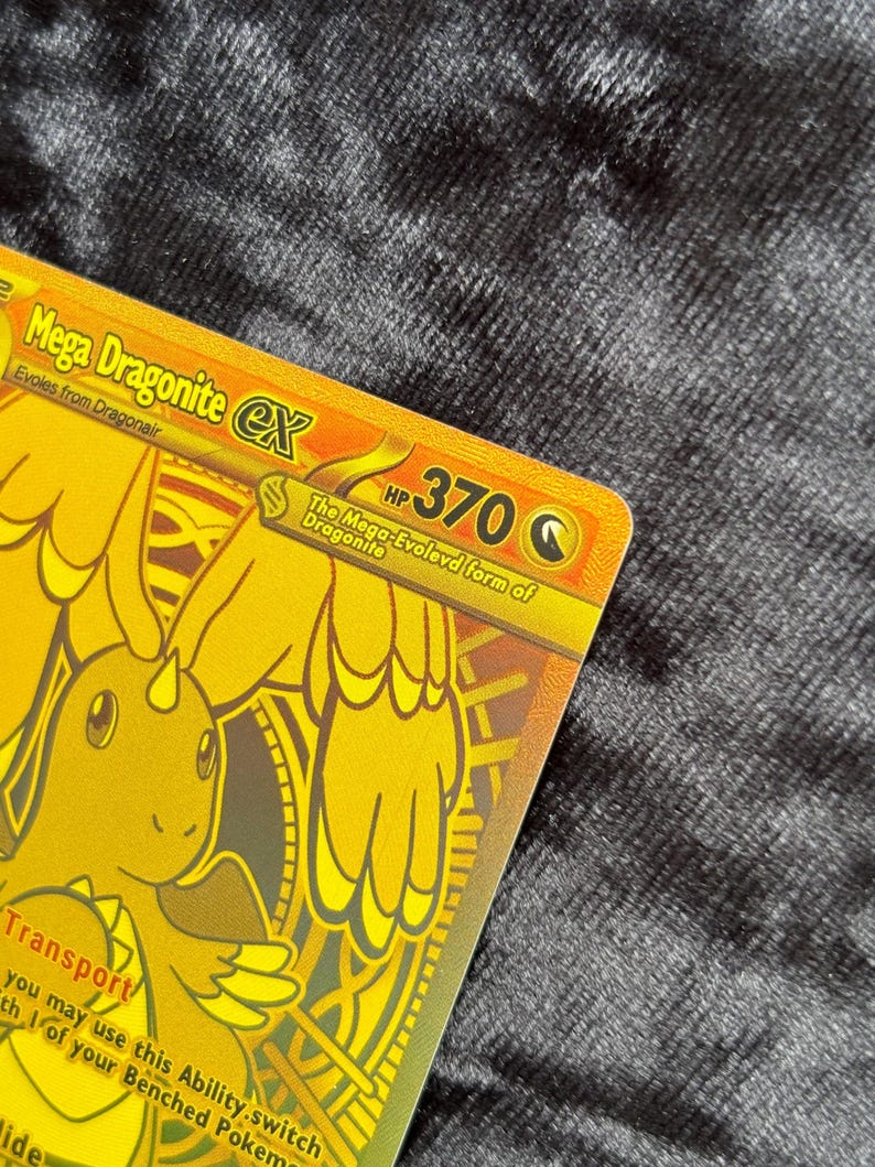 K&ouml;nnte beinhalten: Eine goldene Mega Dragonite EX Sammelkarte. Die Karte zeigt eine goldene Illustration eines drachenartigen Wesens mit dem Text "Mega Dragonite EX" und "HP 370". Die Karte enth&auml;lt auch den Text "Evolves from Dragonair".