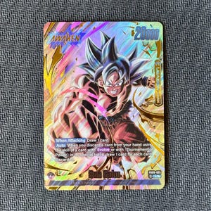 May include: A holographic trading card featuring an illustration of Son Goku with silver hair in a dynamic fighting pose. The card displays the text AWAKEN, 20000, and game instructions. It includes the identifier F009-025 and a gold-toned border design.