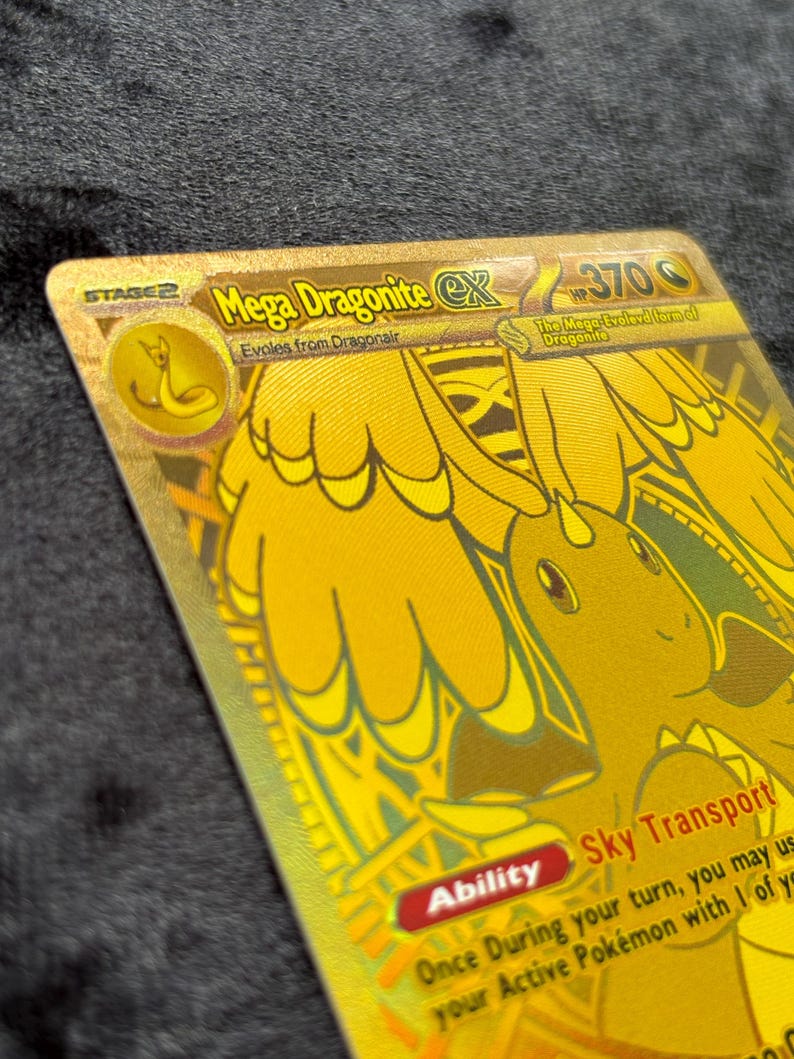 K&ouml;nnte beinhalten: Eine goldfarbene Mega Dragonite EX Sammelkarte. Die Karte zeigt eine detaillierte Illustration eines drachenartigen Wesens mit dem Text "Mega Dragonite EX" und "Sky Transport". Die Karte hat eine Stufe 2-Bezeichnung und 370 HP.