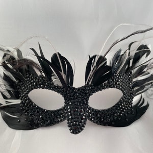 Máscara Cruella DeVille De Vil com penas em camadas e strass pretos.