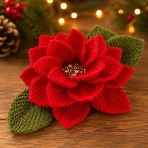 May include: A crocheted poinsettia flower with vibrant red petals and a textured center featuring small gold beads. The flower is accented by two dark green crocheted leaves, creating a detailed floral piece with a soft, yarn-based texture.