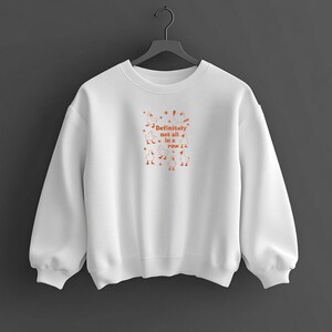 May include: White sweatshirt with the text "Definitely not all in a row" in orange, along with orange illustrations of geese and stars. The sweatshirt has a crew neck and long sleeves.