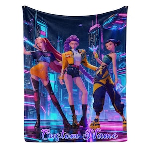 May include: A plush, dark blue blanket featuring a vibrant illustration of three animated figures in a futuristic cityscape. The figures are dressed in stylish outfits with yellow, orange, and blue accents. The words "Custom Name" are written in cursive at the bottom.