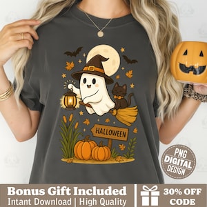 Puede incluir: Camiseta gris oscuro con un diseño de Halloween. El diseño incluye un fantasma amigable con un sombrero de bruja, un gato negro en una escoba, calabazas y la palabra "HALLOWEEN" en un letrero. Una luna llena y murciélagos en el fondo.