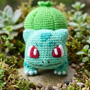 Puede incluir: Un peluche tejido a mano en forma de criatura con un cuerpo de color verde menta claro, un gran bulbo verde redondeado en la espalda y ojos rojos con pupilas blancas. La figura presenta pequeñas orejas puntiagudas, manchas y garras blancas.