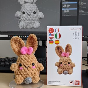 Könnte beinhalten: Ein braunes Häschen-Spielzeug aus Häkelarbeit mit einer rosa Schleife, schwarzen Augen und einem grauen Boden. Das Spielzeug steht auf einem transparenten Ständer. Daneben eine Schachtel mit dem Bild des Spielzeugs und japanischem Text.