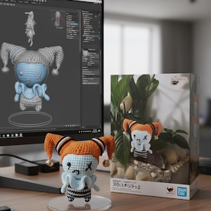 Peut inclure: Poupée crochetée à la main avec un chapeau orange et noir, un visage bleu et une tenue à carreaux noirs et blancs. La poupée est exposée sur un présentoir transparent. Une poupée similaire est dans une boîte avec des plantes.