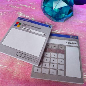 May include: Two square paper note pads featuring retro computer interface designs. One pad displays a Shut Down Windows dialog box with the text Shut down worries. The other pad shows a calculator interface with the text = HAPPY.