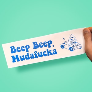 Könnte beinhalten: Ein weißer, rechteckiger Aufkleber mit blauem Text, der "Beep Beep, Mudafucka" lautet. Ein Cartoon-Hund in einem Auto ist ebenfalls in Blau dargestellt. Der Aufkleber wird von einer Hand vor einem türkisfarbenen Hintergrund gehalten.