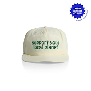Może przedstawiać: Kremowa czapka bejsbolówka z zakrzywionym daszkiem. Na czapce widnieje napis "SUPPORT YOUR LOCAL PLANET" w zielonych literach. Niebieski graficzny wykrzyknik w prawym górnym rogu głosi "CHOOSE YOUR HAT COLOUR!" i "SUBJECT TO AVAILABILITY".