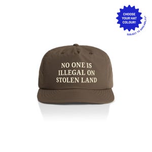 May include: A brown baseball cap featuring the white text "NO ONE IS ILLEGAL ON STOLEN LAND". A blue starburst graphic in the top right corner says "CHOOSE YOUR HAT COLOUR!" and "SUBJECT TO AVAILABILITY".