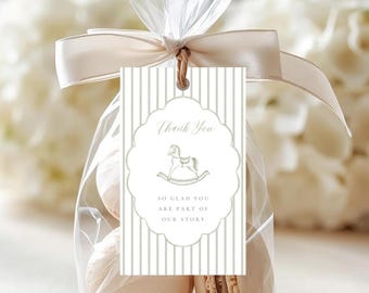 May include: A clear plastic favor bag containing beige macarons, tied with a cream satin ribbon and a rectangular tag. The tag features grey vertical stripes, a scalloped oval frame, a rocking horse icon, and the text Thank You SO GLAD YOU ARE PART OF OUR STORY.