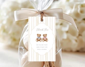 May include: A clear plastic favor bag filled with beige macarons, tied with a cream satin ribbon and a rectangular tag. The tag features vertical beige stripes, two teddy bears with blue and pink bows, and the text Thank You SO GLAD YOU ARE PART OF OUR STORY.