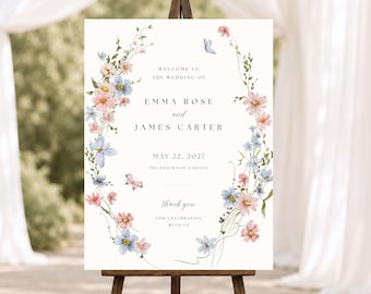 May include: A rectangular wedding welcome sign on a wooden easel featuring a watercolor floral wreath in shades of pink and blue with small butterflies. The text reads: WELCOME TO THE WEDDING OF EMMA ROSE and JAMES CARTER MAY 22, 2027 THE ROSEWOOD GARDENS thank you FOR CELEBRATING WITH US.